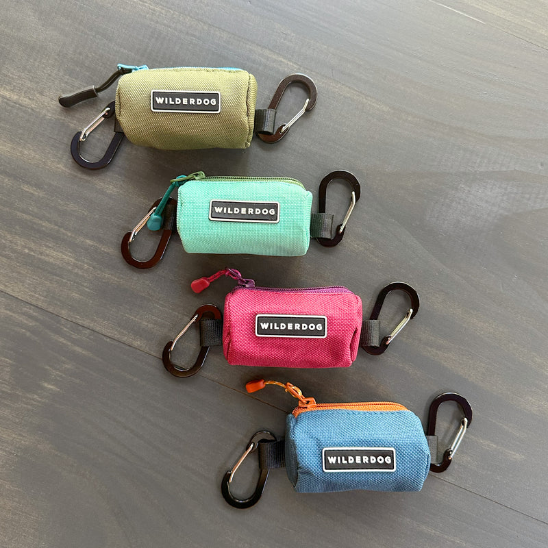 Four colorful dog poop bag holders with carabiners, labeled "WILDERDOG" ideal for leash attachments